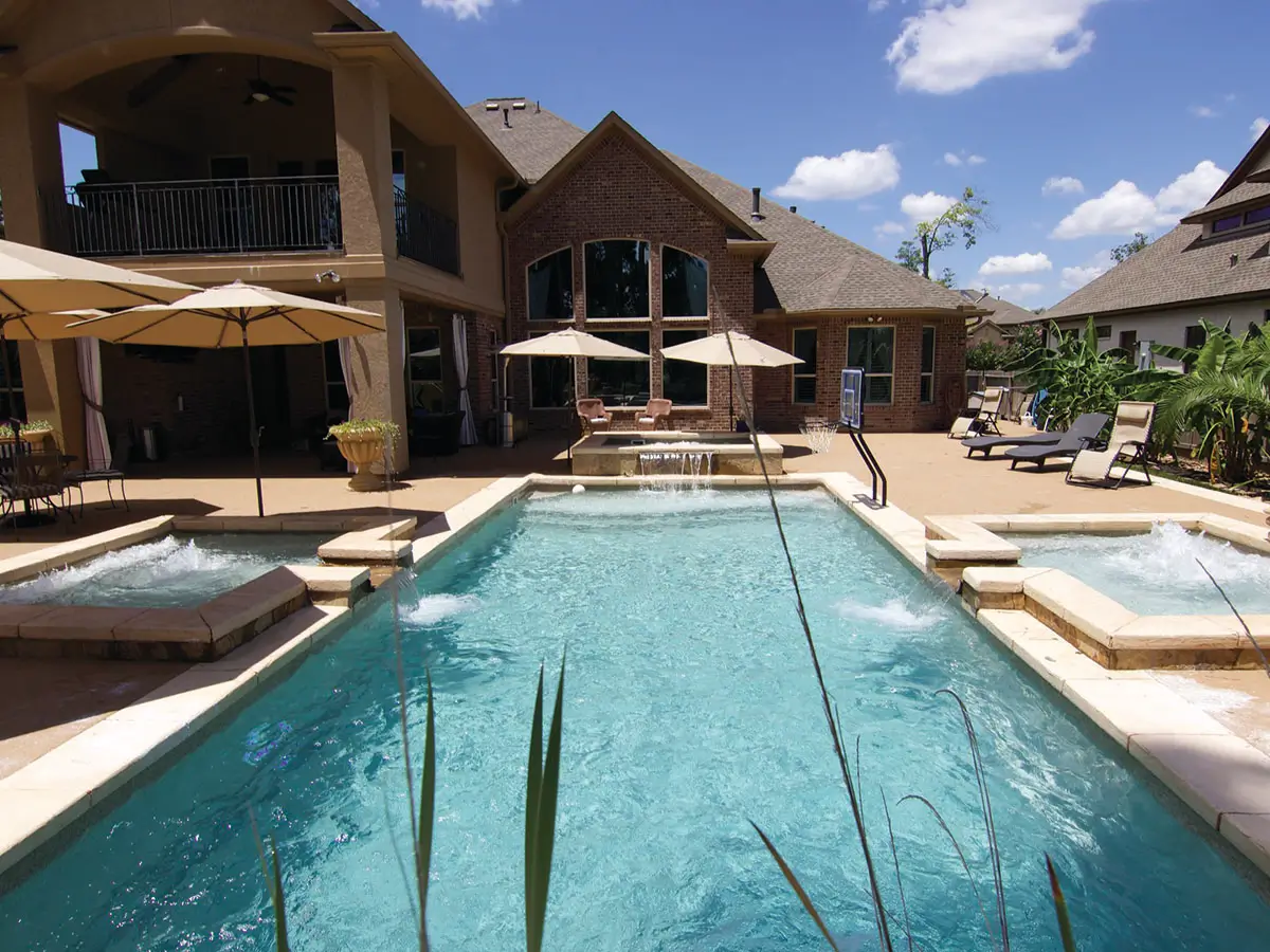 Backyard fiberglass swimming pool with pebble beach design surrounded by lawn and patio, illustrating a custom pool installation in Tennessee.