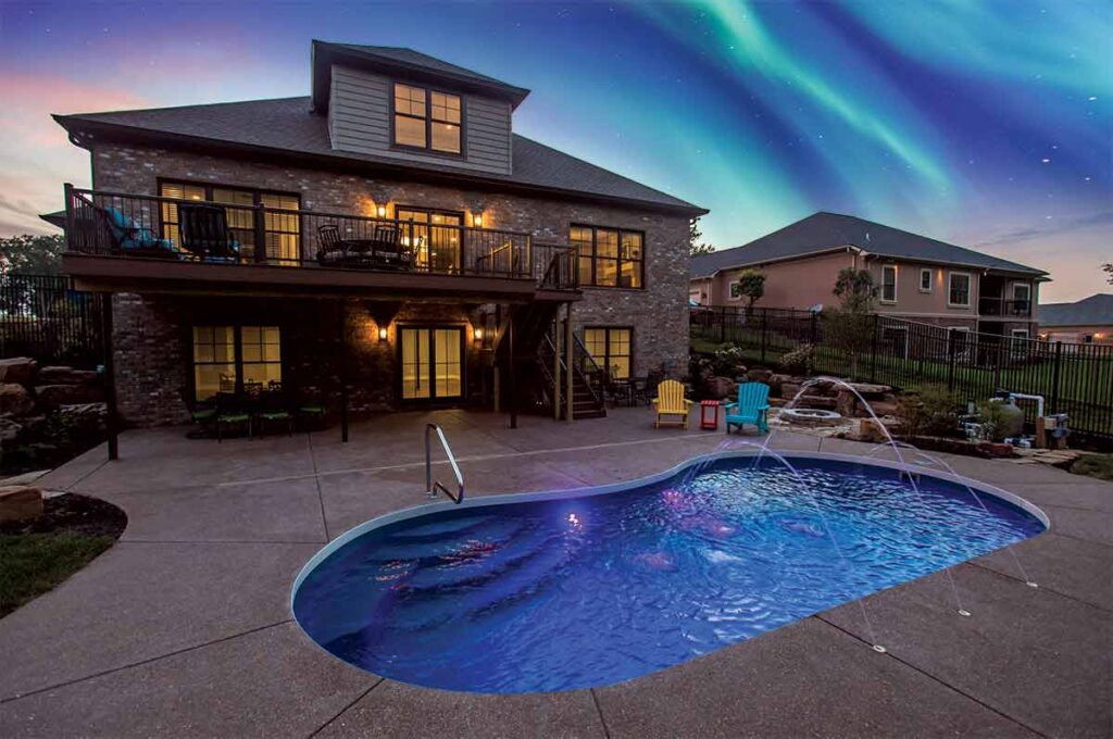 A picture of a backyard fiberglass pool with a lit up home at twilight