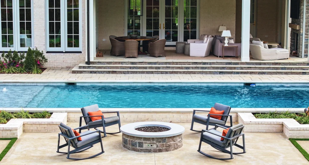 Pool-side chairs next to a pool and a pool fire pit