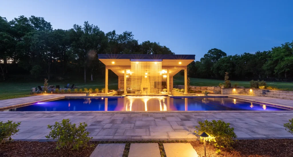 Night view of a swimming pool with surrounding stone paving and minimalist landscaping, highlighting low‑maintenance hardscape ideas around a pool.