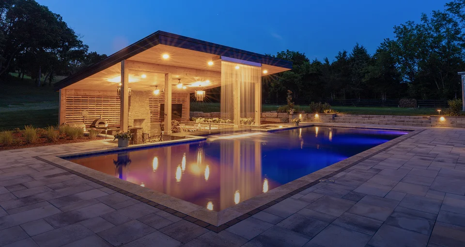 A picture of a fiberglass pool at night with a lit-up outdoor pool enclosure