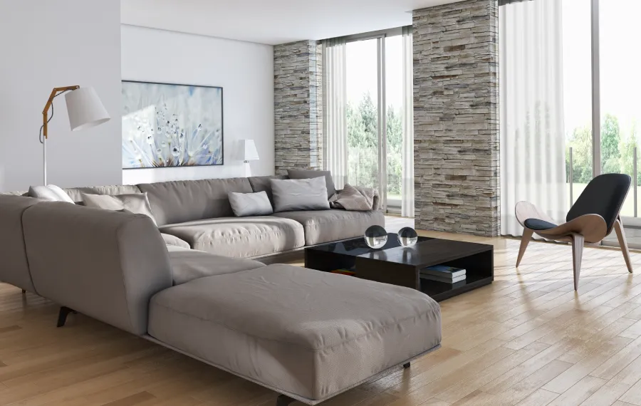 Modern living room with a large gray sectional sofa, stone accent wall, and floor-to-ceiling windows. Soft lighting creates a warm, inviting atmosphere.